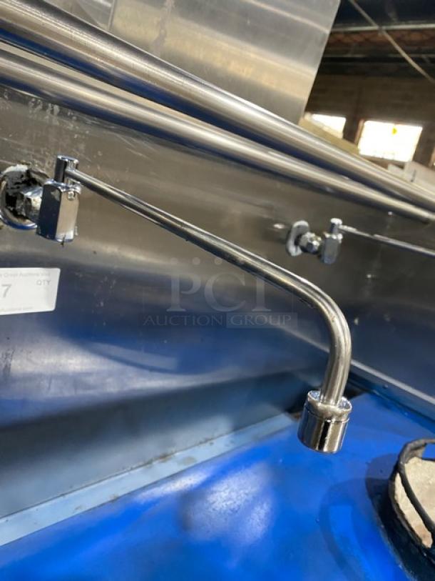 Commercial stainless steel gas-powered 2-burner Chinese wok range with backsplash, dual swivel spout faucet, on legs.