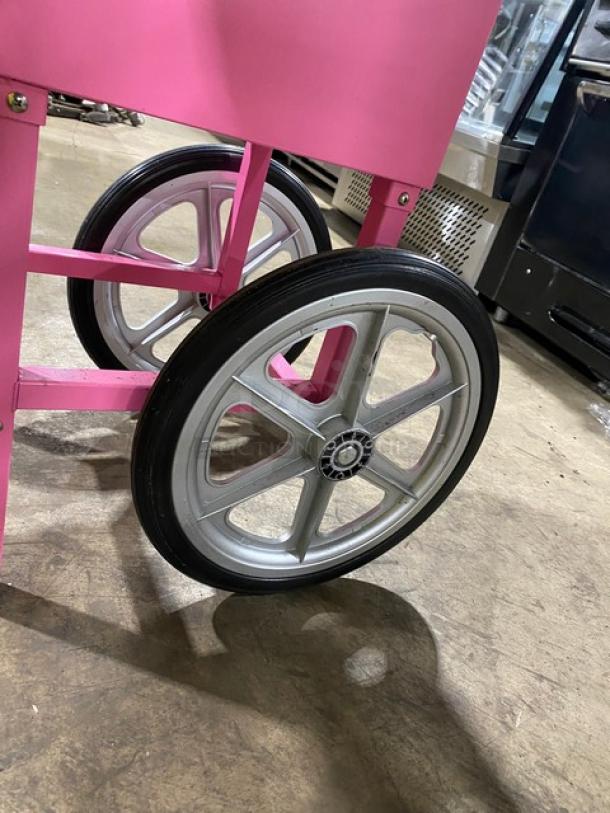 Olde Midway Spin-2000 hot-pink cotton candy machine on wheels, shown with silver spokes and sturdy black tires.