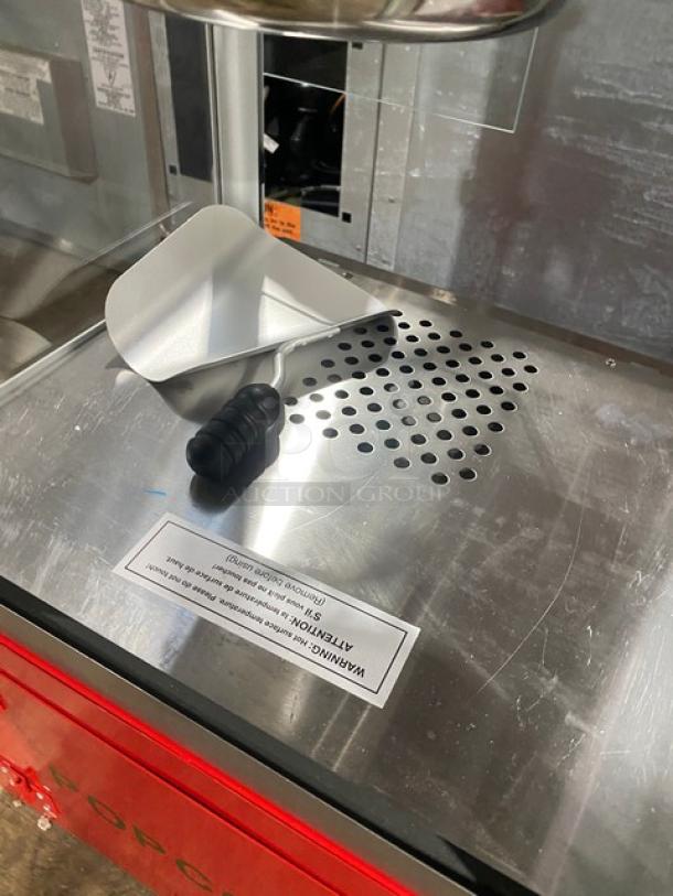 Carnival King red stainless steel popcorn machine with removable kettle, popcorn scoop, and cabinet-style storage.