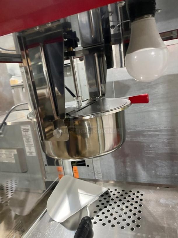 Carnival King red stainless steel popcorn machine with removable kettle, popcorn scoop, cabinet storage, and stand legs.