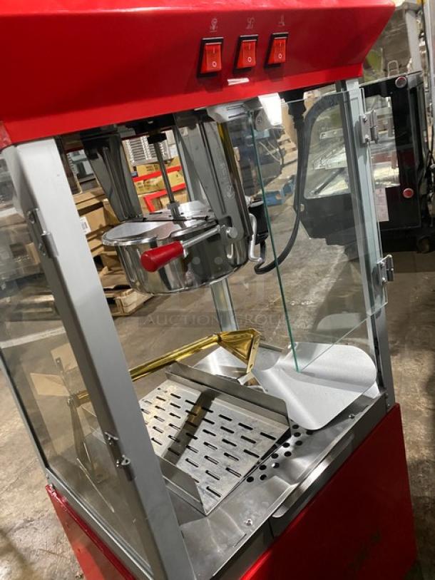 Carnival King red stainless steel popcorn machine with removable kettle, popcorn scoop, and cabinet-style storage.