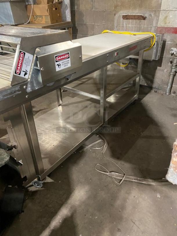 Rondo floor style belt conveyor system, stainless steel, used condition, with warning labels and integrated shelving.