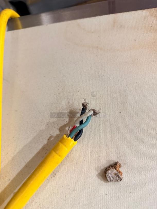 Frayed yellow power cord with exposed wires, suggesting repair needed. Nearby debris on the surface.