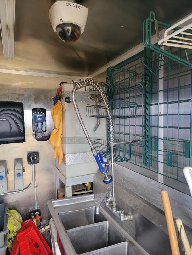 Interior of 2021 Diamond Cargo 24' mobile kitchen trailer featuring a stainless steel triple sink, shelving, and plumbing fixtures.