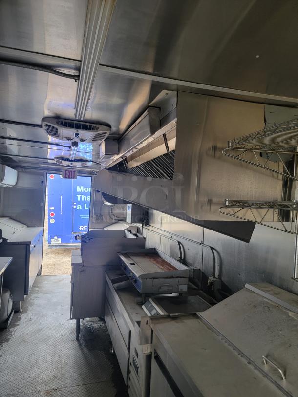 Diamond Cargo 24' mobile kitchen trailer interior, featuring stainless steel equipment and storage racks, showcasing professional cooking setup.