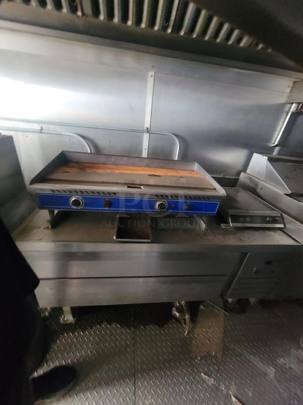 Mobile kitchen interior in Diamond Cargo trailer with stainless steel counters, grill, and ventilation hood, showing signs of use.