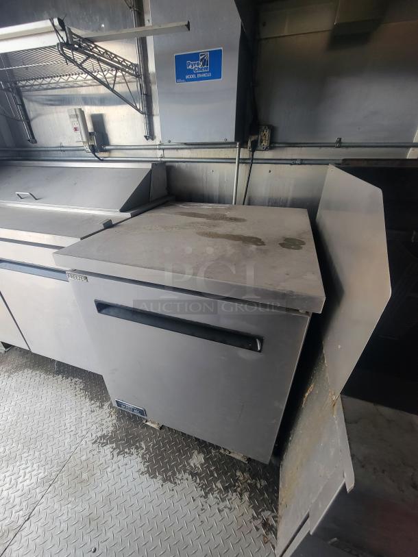 Interior view of a 2021 Diamond Cargo 24' mobile kitchen trailer, featuring professional-grade stainless steel equipment and a Pyro-Chem Model EMACLUD fire suppression system. Ideal for high-volume culinary operations.