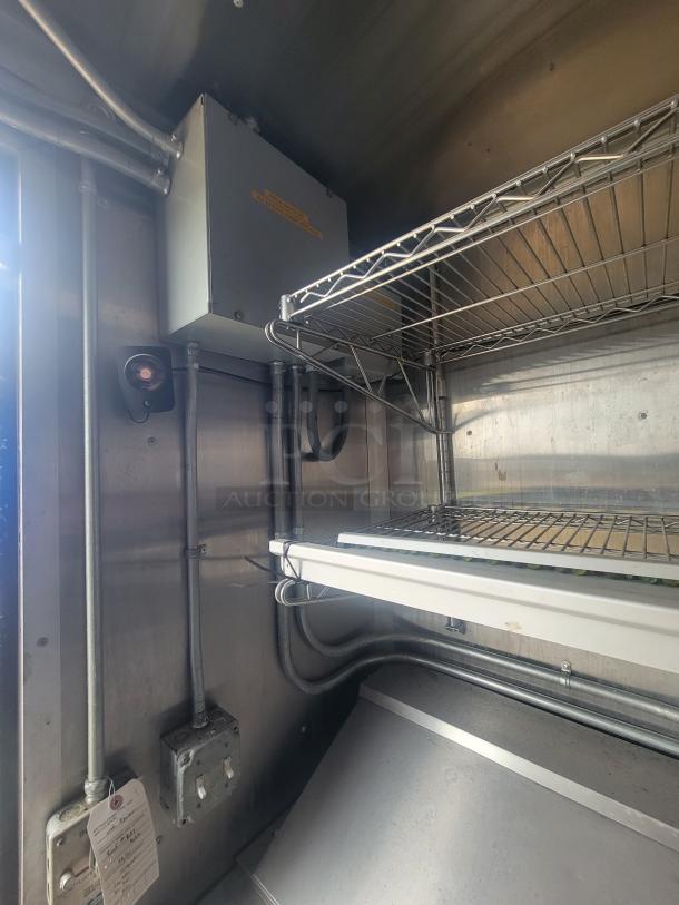 Interior view of a 2021 Diamond Cargo 24' mobile kitchen trailer showing metal wiring shelves, electrical panel, and a switch box.