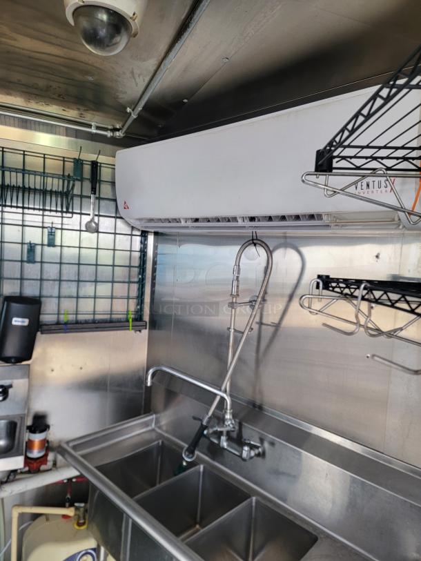 Haulmark 24' mobile kitchen interior with stainless steel sink, Ventus inverter for climate control, and wire shelving.