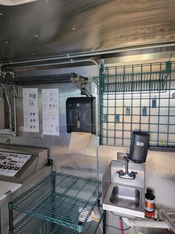 Haulmark 24' mobile kitchen interior with metal shelving, Ecolab soap dispenser, sink, climate control, and appliance setup.