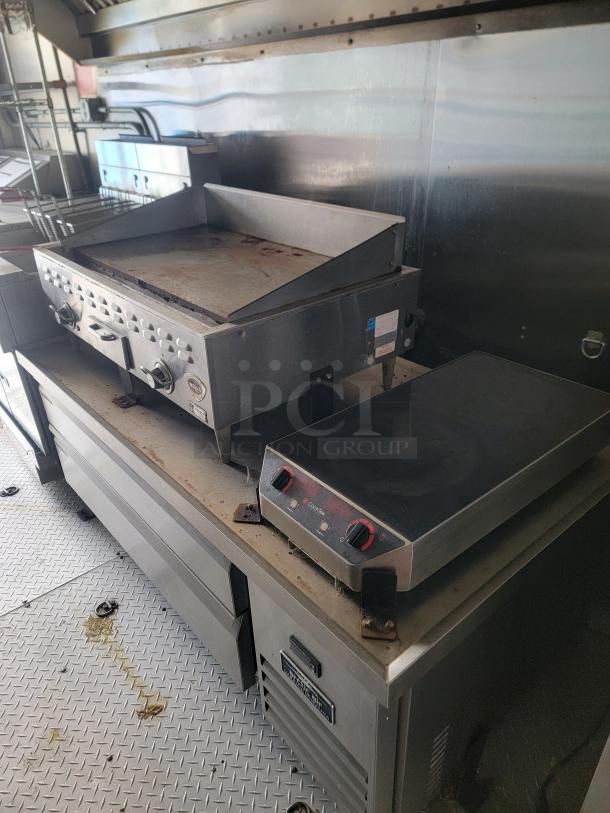 24' Haulmark mobile kitchen interior with grill and stovetop, featuring premium cooling drawers and stainless steel surfaces.