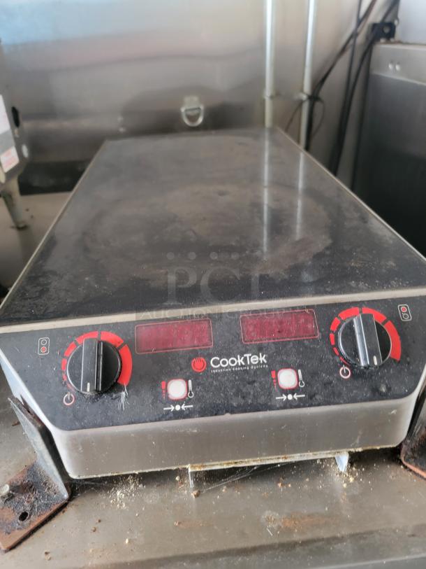 CookTek induction cooktop with dual red control knobs in used condition, part of a fully loaded 24' Haulmark mobile kitchen.