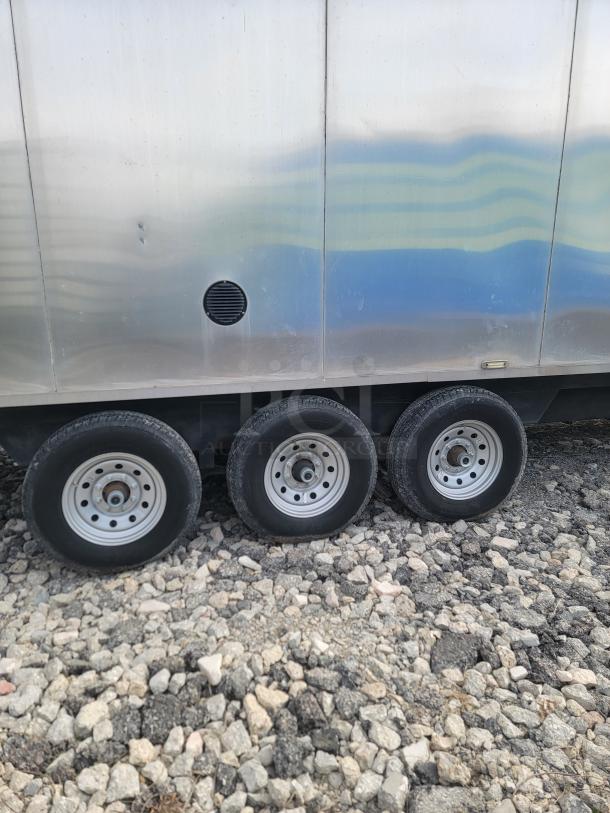 Triple axle of 2021 Texino FD-306 stainless-steel mobile kitchen on rocky ground, showing robust wheels and exterior.