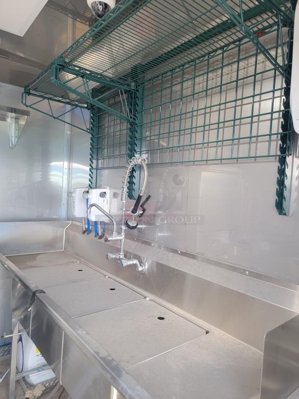Stainless steel kitchen sink area in 2021 Texino FD-306 mobile kitchen, featuring a triple sink setup with overhead green wire shelving.