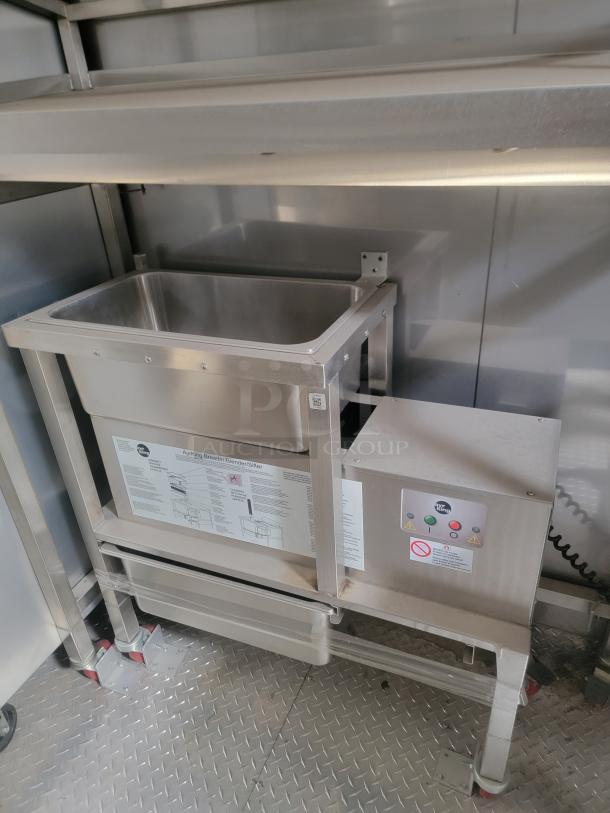 Stainless steel mobile kitchen interior with a commercial breader/blender/sifter on a metal floor. Needs cleaning.