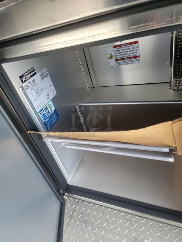 Interior of a 2021 Texino FD-306 mobile kitchen showing True refrigeration unit with visible warning labels and diamond plate flooring.