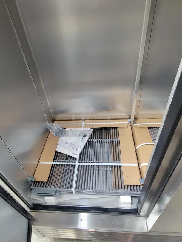 Interior of True refrigeration unit in Texino FD-306 mobile kitchen, showing new wire shelves and instruction manual.