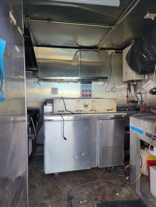 2019 Quality Cargo 24' mobile kitchen interior; features Garland 4-burner range, storage units, and Rinnai water heater; needs cleaning.