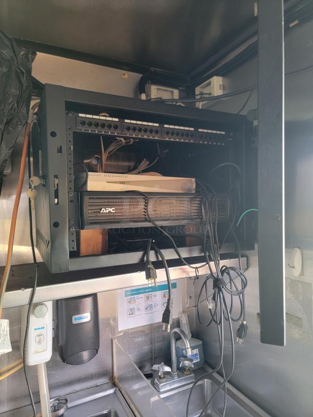 Interior of a 2019 Quality Cargo 24' Mobile Ghost Kitchen. Features visible networking equipment, APC power unit, sink, and Ecolab dispenser. Needs cleaning and maintenance.