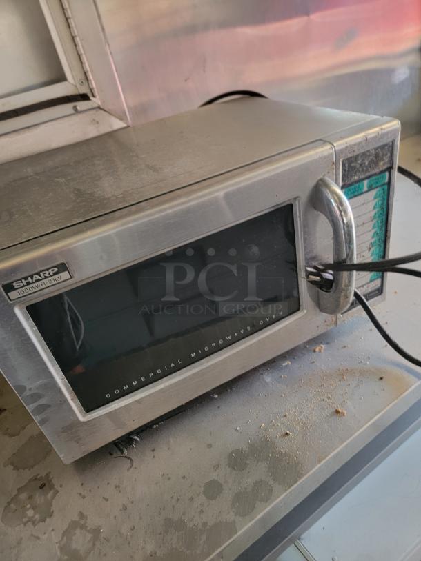 Sharp commercial microwave model R-22, stainless steel, showing signs of use, on countertop with visible crumbs.
