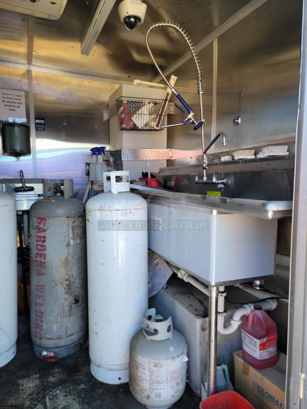 2021 Diamond Cargo 24' mobile kitchen interior with propane tanks, sink, Avigilon camera, and industrial sprayer in stainless setup.