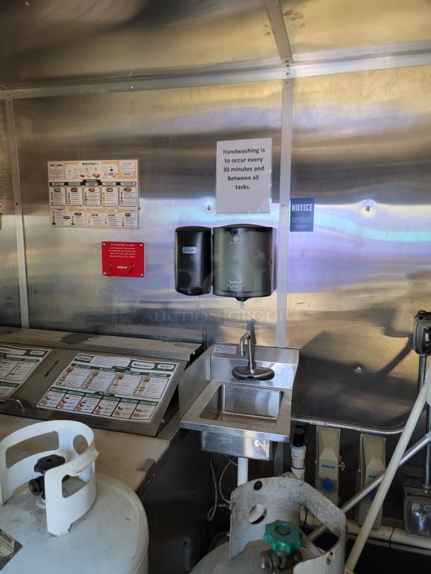 Interior view of a 2021 Diamond Cargo 24' mobile kitchen, showcasing a handwashing station, sanitizer dispensers, and propane tanks.