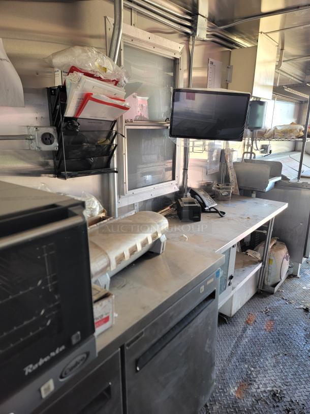 Interior of 2021 Diamond Cargo 24' mobile kitchen, featuring equipment and storage. Visible shelves hold supplies.