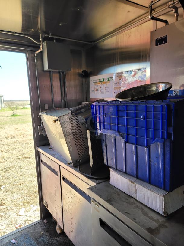 Interior of a 2021 Diamond Cargo 24' mobile kitchen, featuring stainless steel appliances, blue storage bins, and Freezer unit.