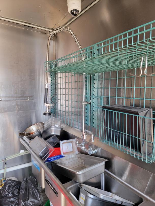 Interior of 2021 Diamond Cargo 24' mobile kitchen showing stainless steel sink, storage shelves, and various kitchen utensils.