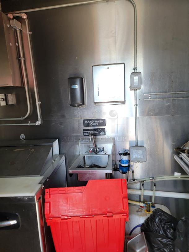 Inside view of a 2021 Diamond Cargo 8.5 x 24 TA mobile kitchen with hand wash sink, soap dispenser, and pipes visible.