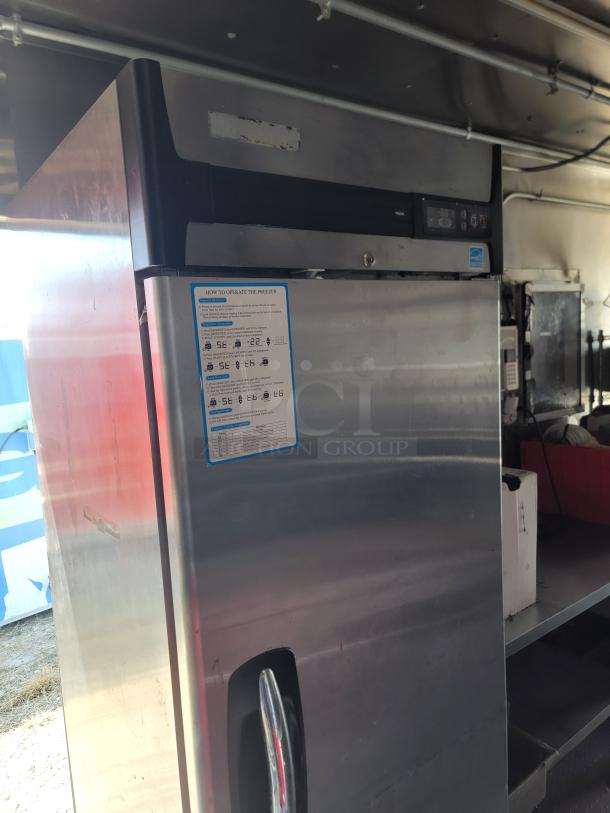 Stainless steel commercial refrigerator inside 2021 Diamond Cargo mobile kitchen, featuring operation instructions and control panel.
