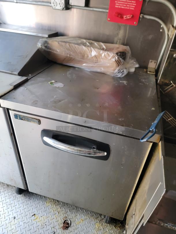Interior view of Diamond Cargo mobile kitchen with steel counter and storage. Light wear, visible Ansul system label above counter.