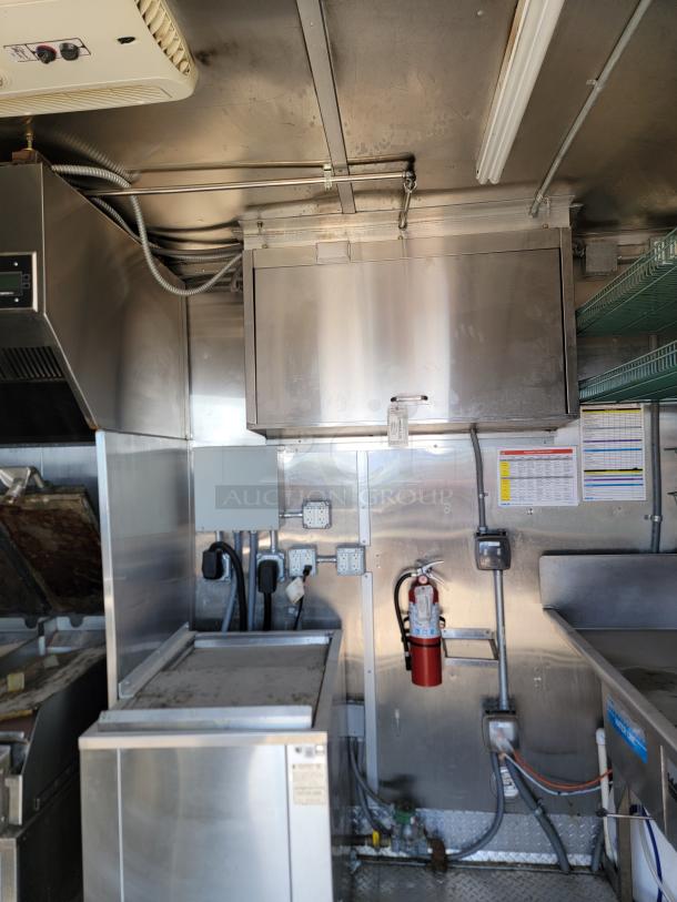 2021 Rock Solid Cargo 28’ mobile kitchen interior, featuring stainless steel surfaces, a ventilation hood, and a fire extinguisher.
