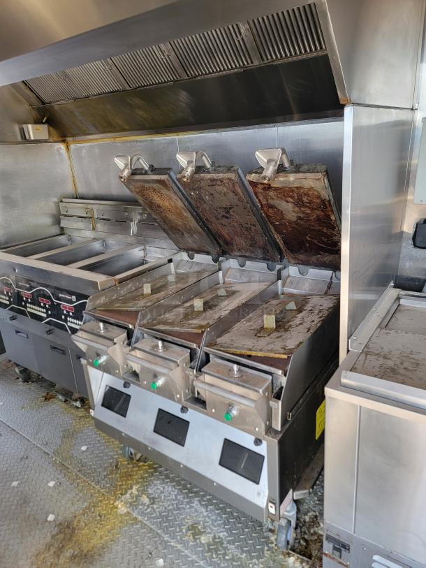 Interior of 2021 Rock Solid Cargo mobile kitchen showing three industrial grills, ventilation hood, and metal flooring.
