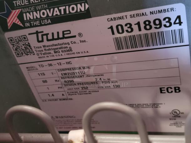 Label showing True Manufacturing Co., model TD-36-12-HC, serial number 10318934, made in the USA. Details include voltage, refrigerant type R290, and design pressures 252 high side, 130 low side PSIG.