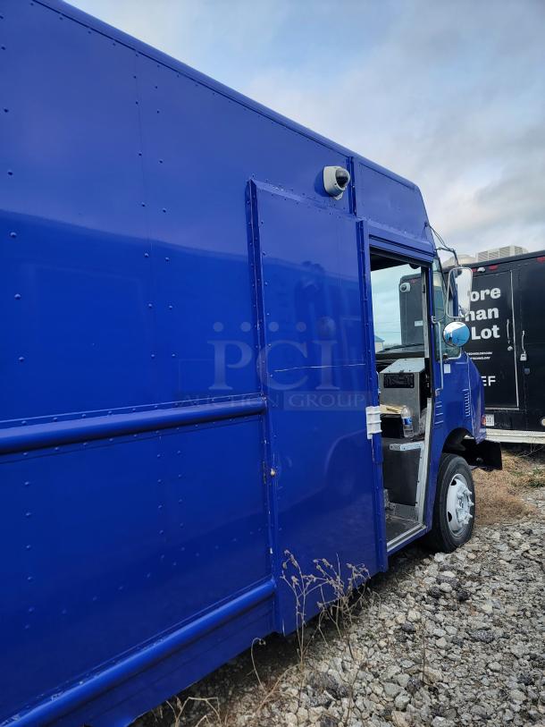 Blue delivery van with side entry door open, parked on gravel. Visible security camera on side, indicating surveillance.
