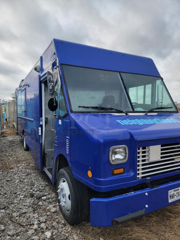 Blue food truck parked outdoors on gravel, featuring a large windshield, side mirrors, and Texas license plate.