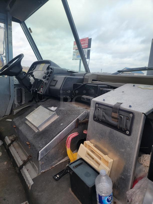 Interior of a vehicle cabin showing steering wheel, dashboard controls, and storage compartments. Worn condition.