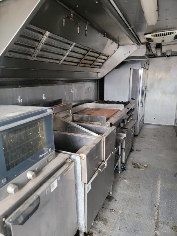 Commercial kitchen equipment inside a food truck, featuring ovens, fryers, and stainless steel counters. Used condition.