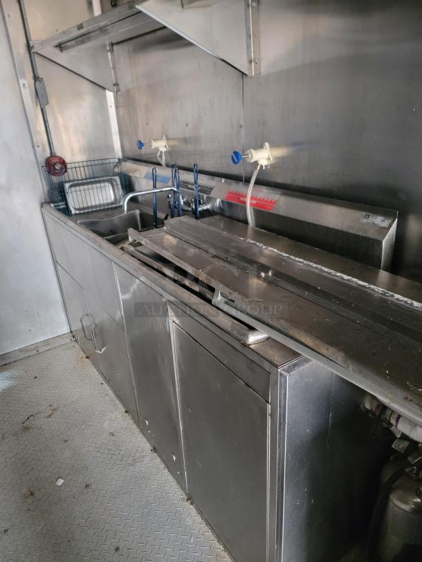 Commercial stainless steel kitchen sink setup with faucet handles, integrated storage, and backsplash in used condition.