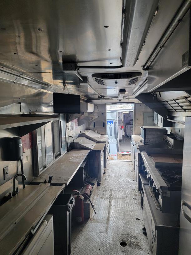 Interior of a stainless steel mobile kitchen with appliances, counters, and safety equipment. Worn condition, shows signs of use.