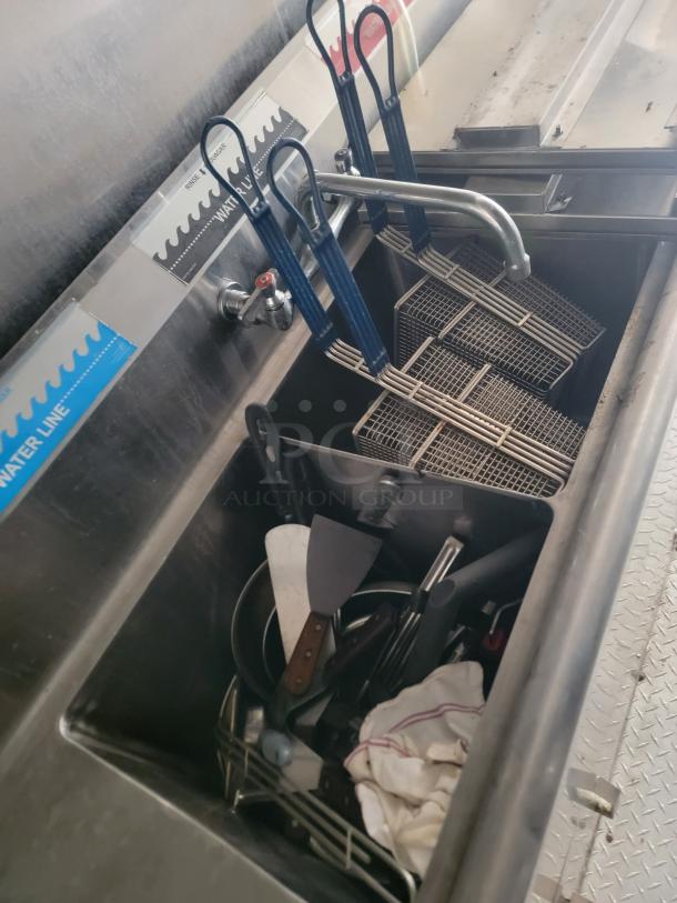 Commercial kitchen sink with attached faucet, multiple fryer baskets with blue handles, and assorted utensils in good condition.