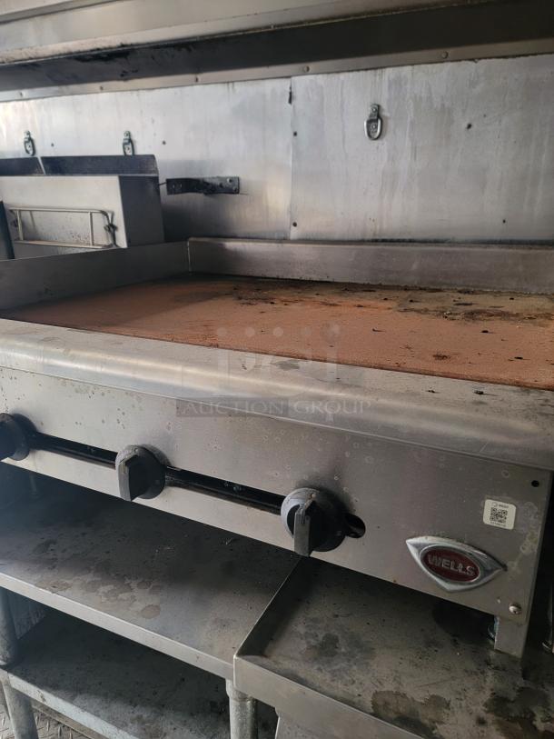 Commercial griddle by Wells; stainless steel with three control knobs, used condition, visible wear and grease.