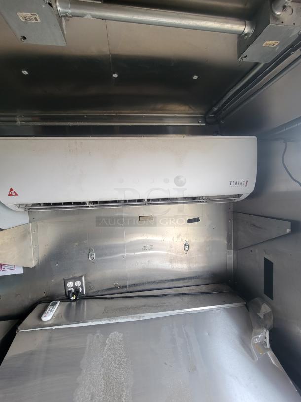 Ventus X air conditioner mounted on stainless steel wall, featuring remote control, visible power outlet, and slight wear.