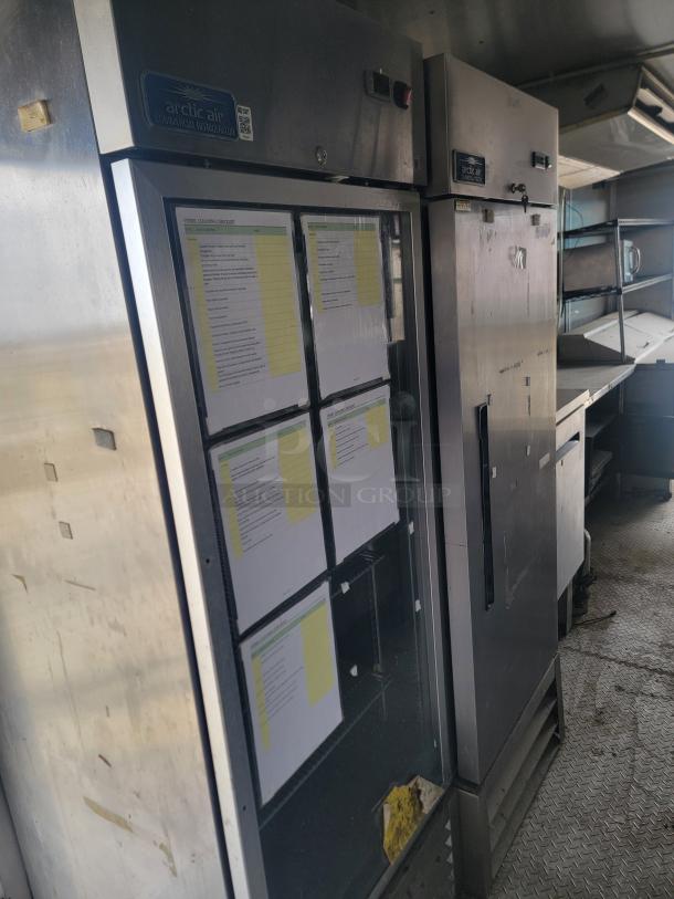 Stainless steel Arctic Air commercial refrigerator with visible cleaning checklists, showing moderate wear.