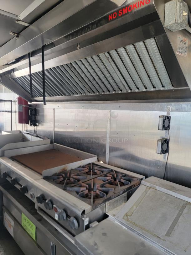 Commercial kitchen with stainless steel exhaust hood and stove featuring burners and griddle, labeled "NO SMOKING."
