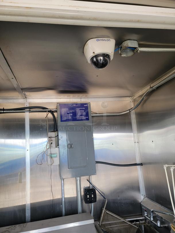 Avigilon dome security camera mounted on a metallic ceiling, near an electrical panel in good condition.