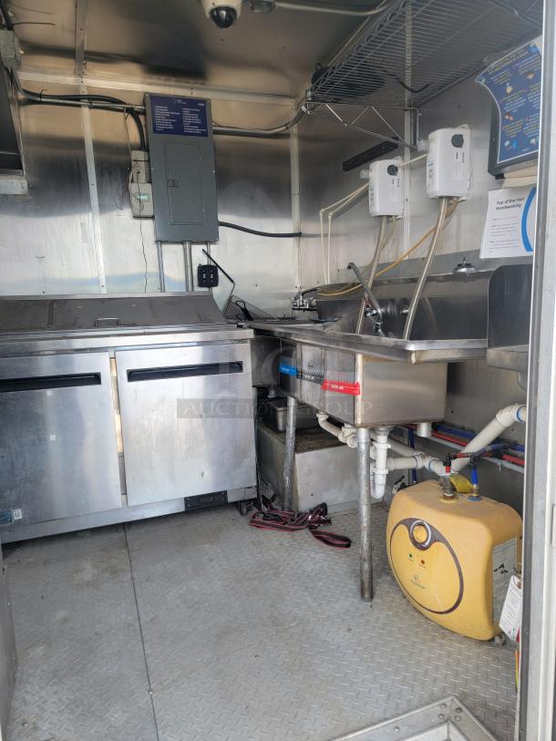 Interior of a stainless steel mobile kitchen unit with a double sink, storage, and heating equipment. Clean and well-maintained.
