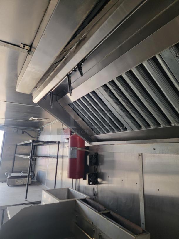 Commercial kitchen exhaust hood in stainless steel, includes fire suppression system and shelving. Clean and well-maintained.