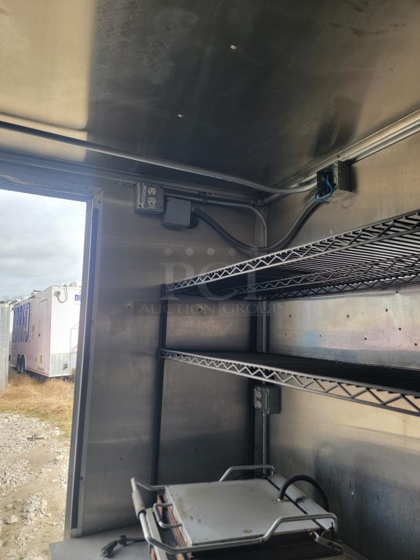 Interior view of a metal storage trailer with wire shelving and electrical outlets. Shelves in good condition, suitable for storage or equipment setup.